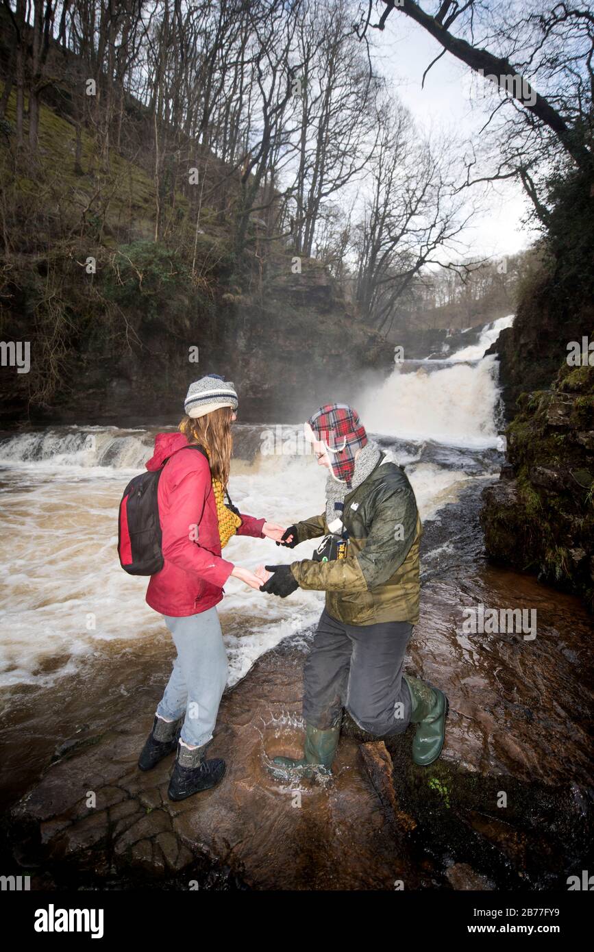 Les marcheurs marchent soigneusement sur les rives de la rivière Mellte au Sgwd Fias Clund-Gwyn tombe près de Pontnedfechan dans les Brecon Beacons, Pays de Galles, Royaume-Uni Banque D'Images
