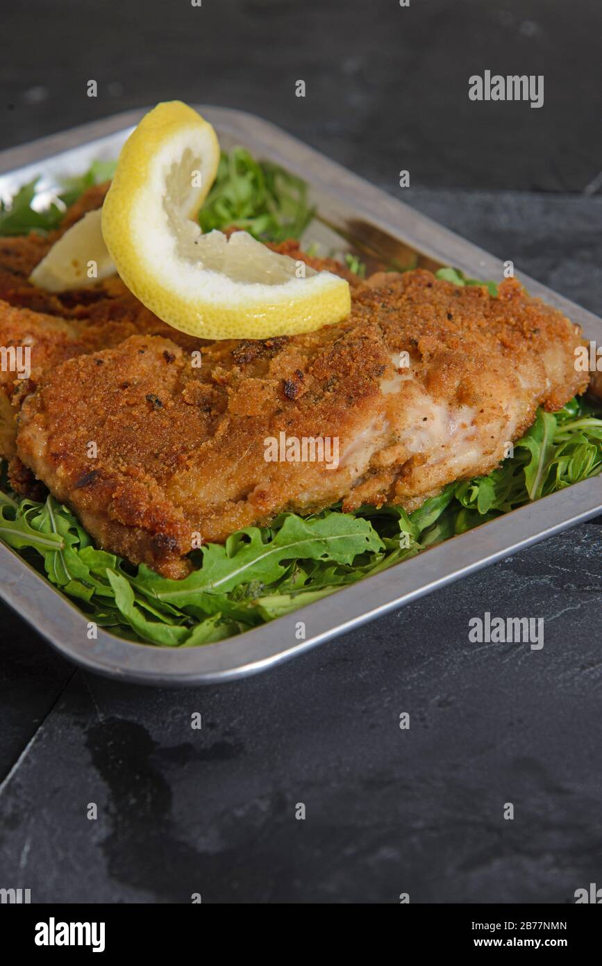 Steak de poulet pané et frit avec une tranche de citron sur un lit de salade fraîche - photo studio verticale Banque D'Images