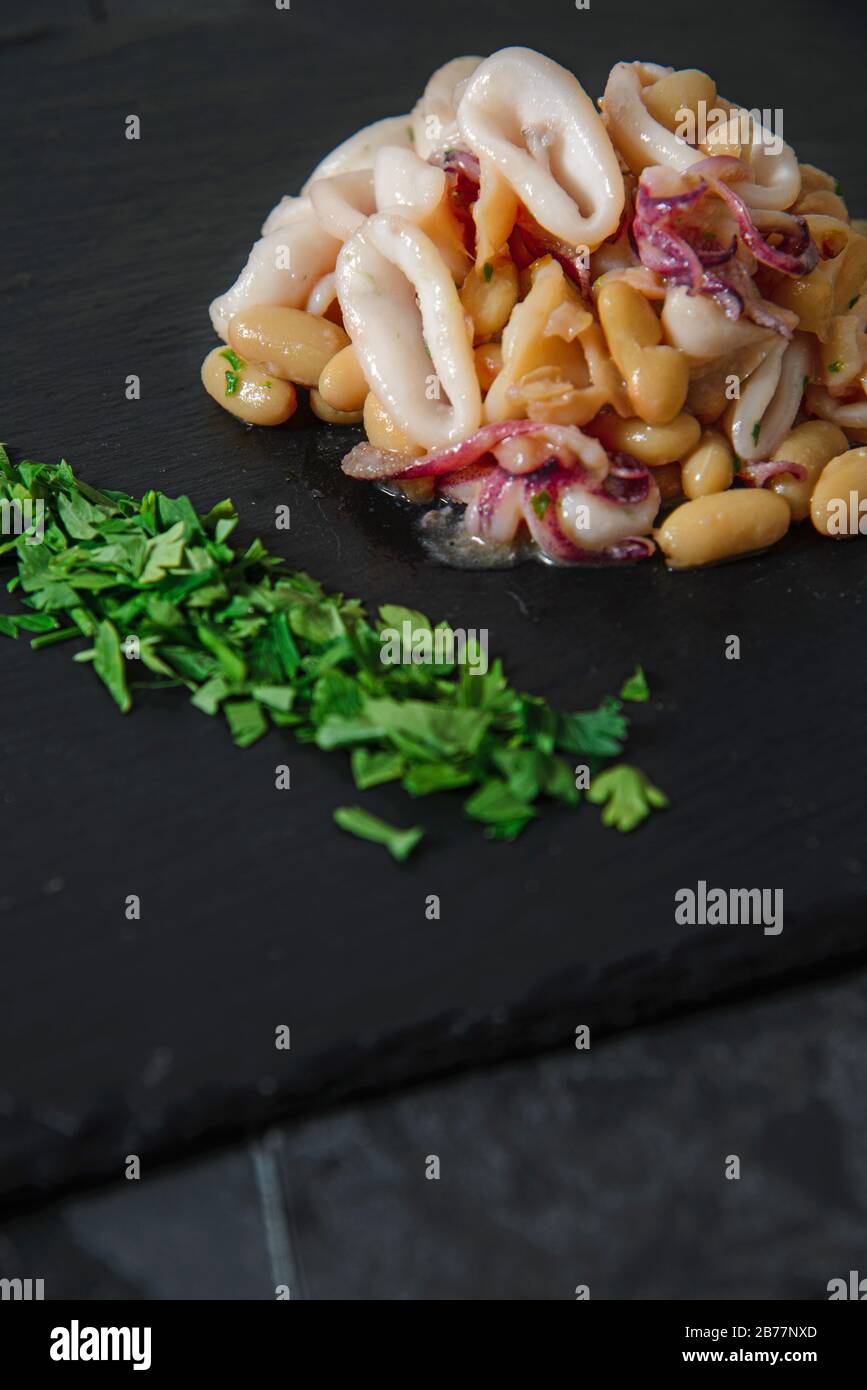 Haricots et calmars frais sur plaque en pierre noire - photo studio verticale Banque D'Images
