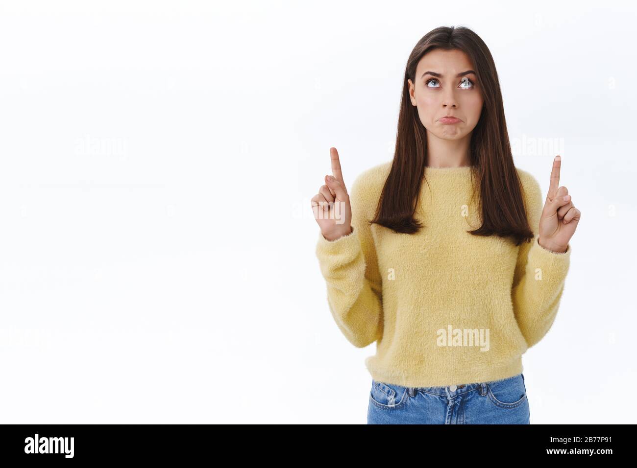 Jaloux et contrarié adorable petite fille brunette tirant le visage triste, grimaçant et regardant pointer les doigts vers le haut avec regret émotion, n'ont pas quelque chose elle Banque D'Images