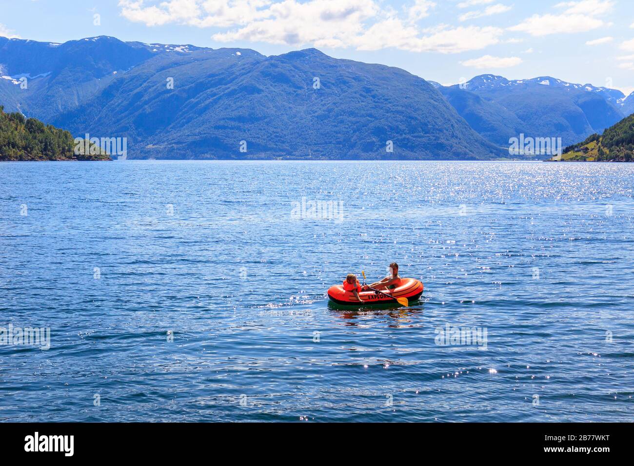 Deux enfants à bord d'un bateau gonflable, aviron dans les fjords de l'ouest de la Norvège. Grandes montagnes en arrière-plan. Banque D'Images