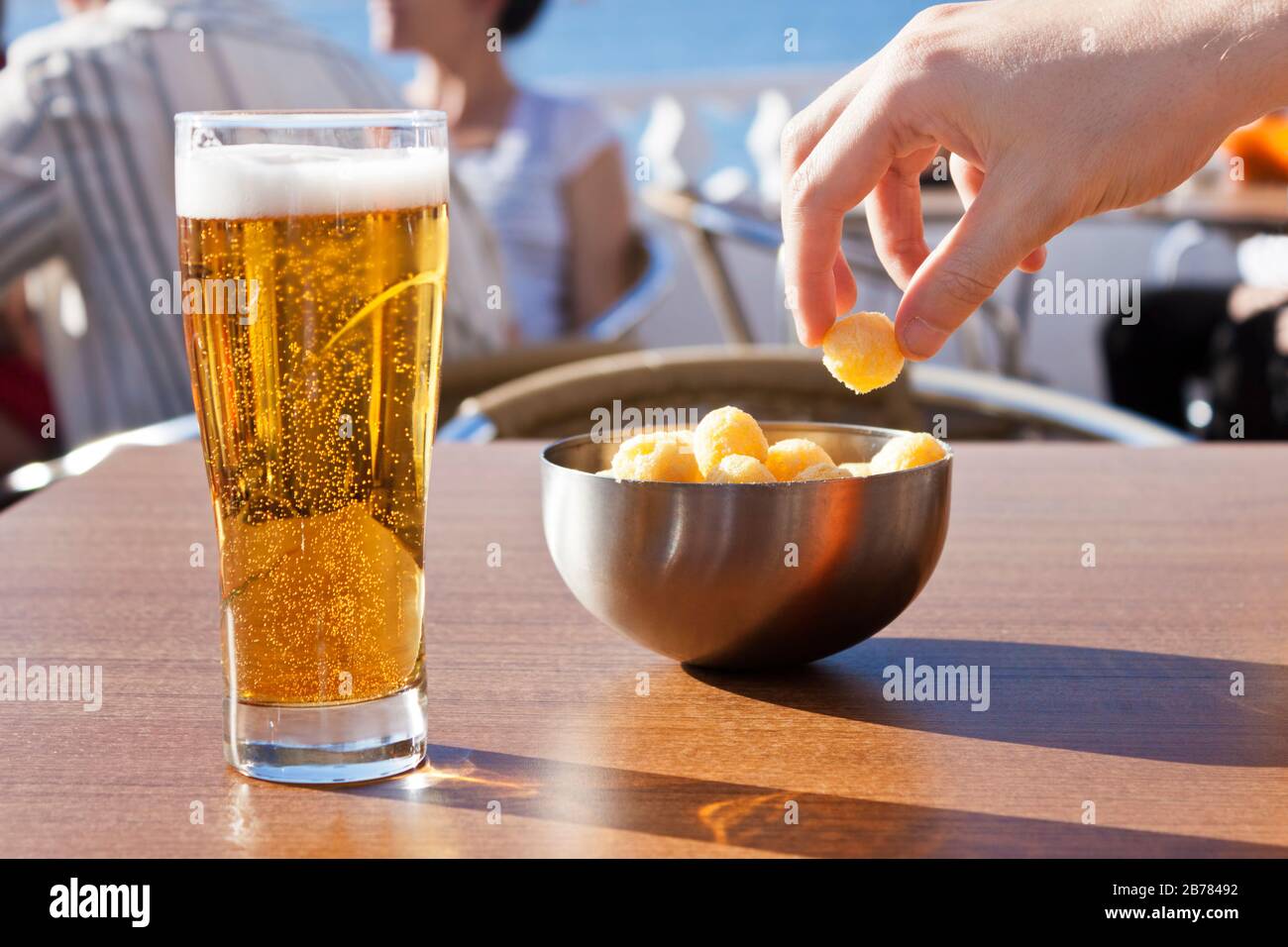 Une cueillette à la main des collations dans un bol et une bière dans une table d'une terrasse près de la mer, dans un beau jour d'été. Banque D'Images