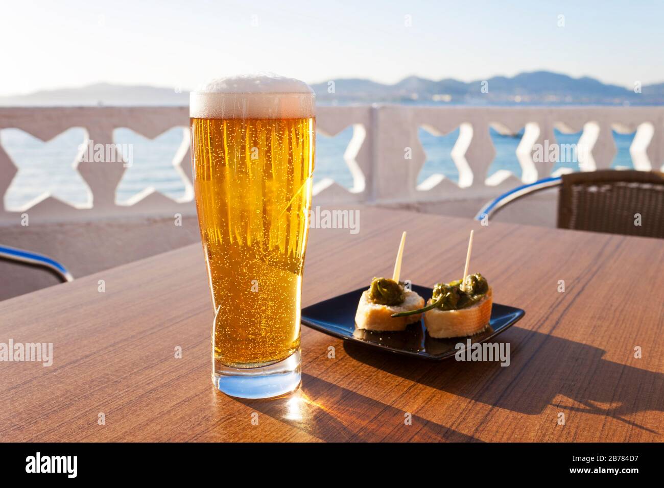 Verre de bière et une assiette de poivrons dans la table d'une terrasse à côté de la mer en Espagne. Banque D'Images