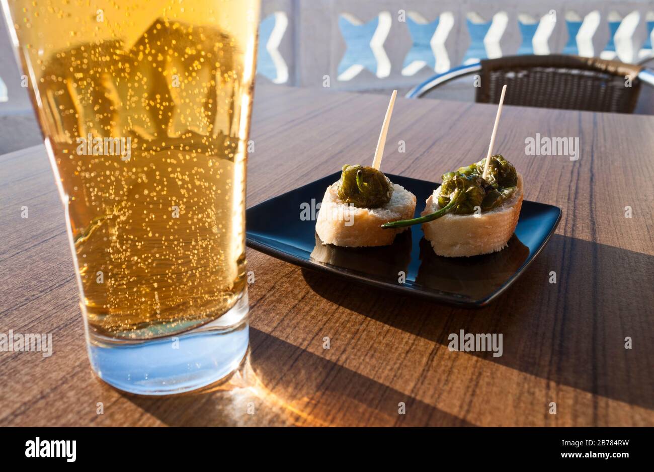Les petits poivrons verts (Padron poivrons) avec du pain dans une assiette avec un verre de bière dans une table d'une terrasse près de la mer. Banque D'Images