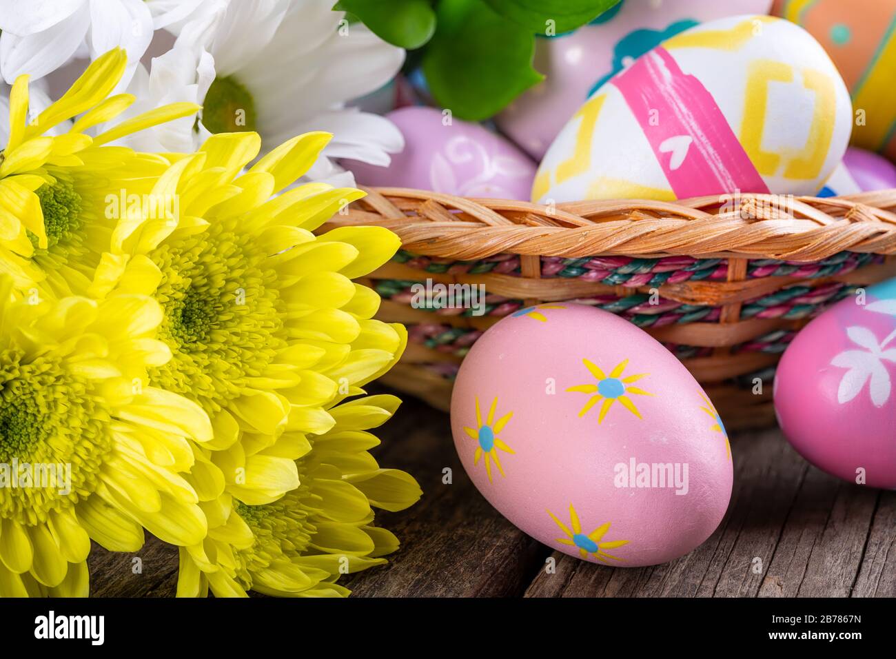 Gros plan d'œufs de pâques colorés sur une table en bois et dans un panier avec de belles fleurs Banque D'Images