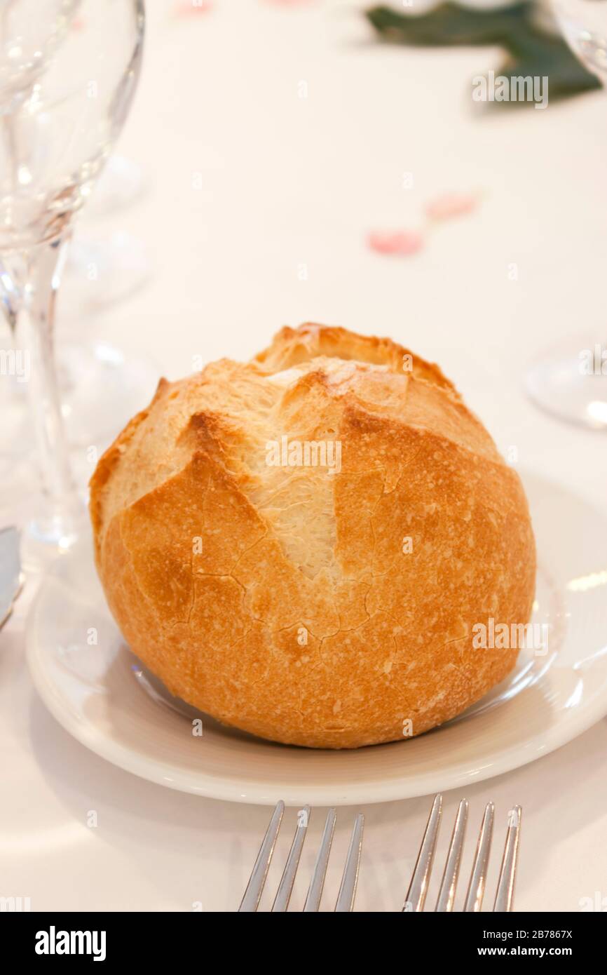 Un petit pain de pain sur une plaque sur une table élégante avec des couverts et verre sur un linge blanc. Banque D'Images