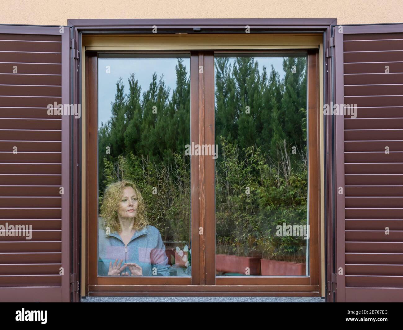 Une femme blonde italienne forcée de rester à l'intérieur à cause de la quarantaine Coronavirus Covid-19, regarde le monde extérieur avec une expression mélancolie Banque D'Images