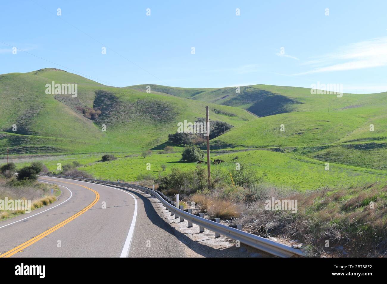 une route sinueuse courbée avec une colline de montagne lumineuse et un ciel bleu Banque D'Images
