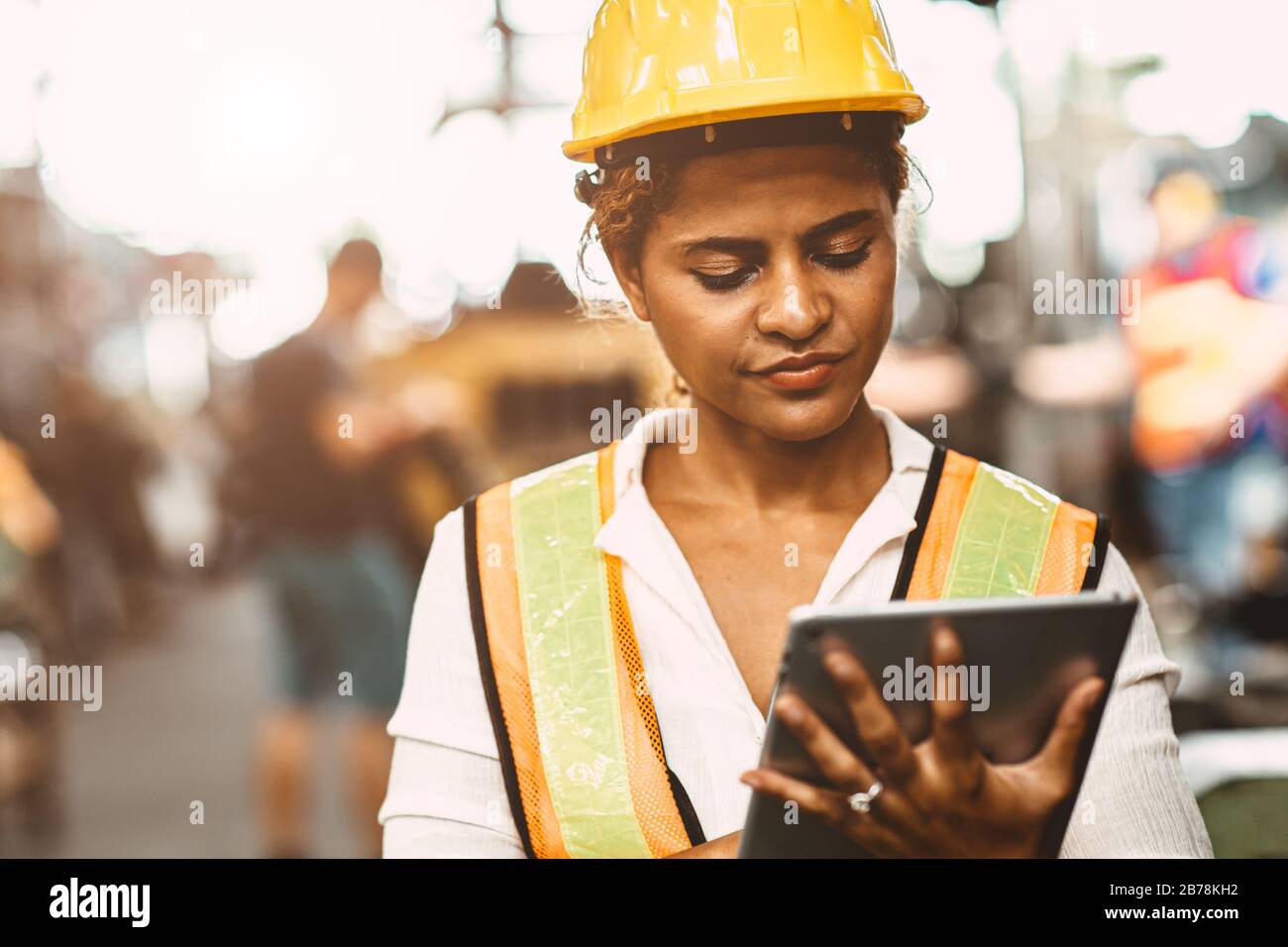 Les femmes américaines travaillant dans l'ingénieur de maintenance de l'industrie lourde se réjouiront de travailler avec un uniforme de sécurité et un casque utilisant une tablette pour contrôler la machine Banque D'Images
