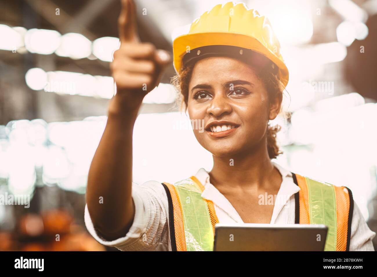 Une dame américaine dans l'ingénieur d'entretien d'usine se réjouit de travailler avec un uniforme de sécurité et un casque de pointage et de sourire pour l'avenir du travailleur nous Banque D'Images