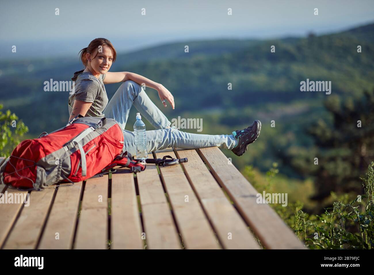 jeune femme assise sur un point de vue élevé en montagne, regardant la caméra. nature, détente, loisirs, remplissage avec concept d'énergie Banque D'Images