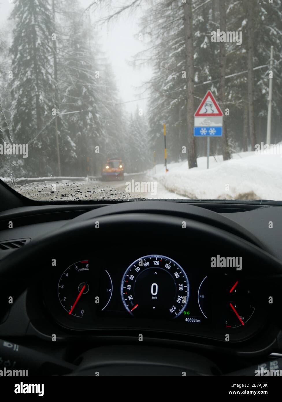 Conduire dans des conditions de route difficiles en journée molle dans les montagnes italiennes vu du point de vue du conducteur, y compris le compteur de vitesse, la route et le véhicule soufflant Banque D'Images
