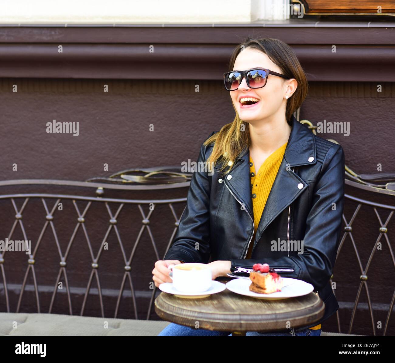 Fille dans des lunettes de soleil près de savoureux gâteau aux baies et café  sur la table sur fond de terrasse marron. Lady boit du café pendant la pause -café. Concept de pâtisserie
