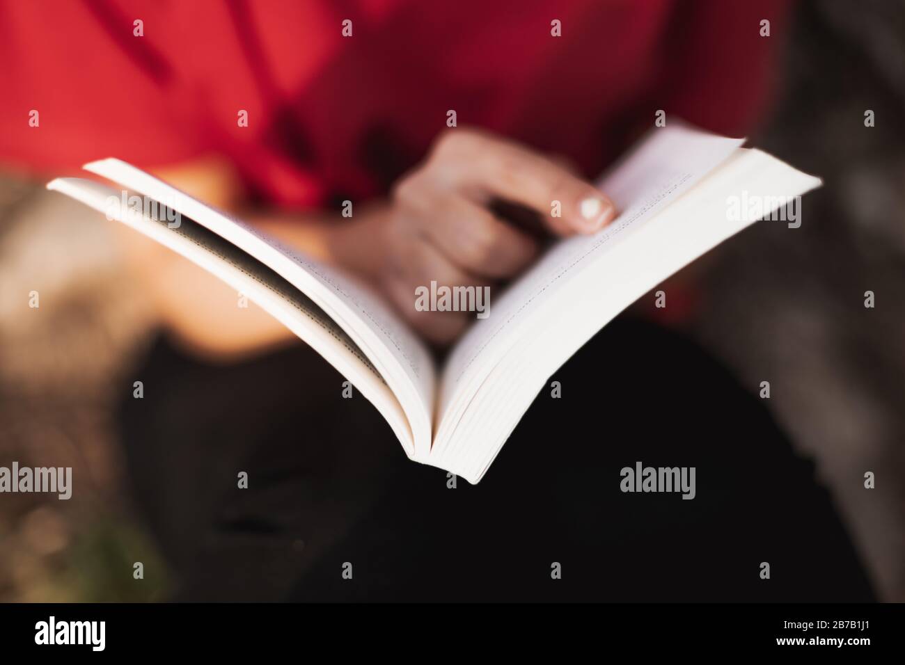 Gros plan d'un livre ouvert juste au milieu par une jeune femme qui pointe son doigt dans un mot de la page. Faible profondeur de champ. Banque D'Images