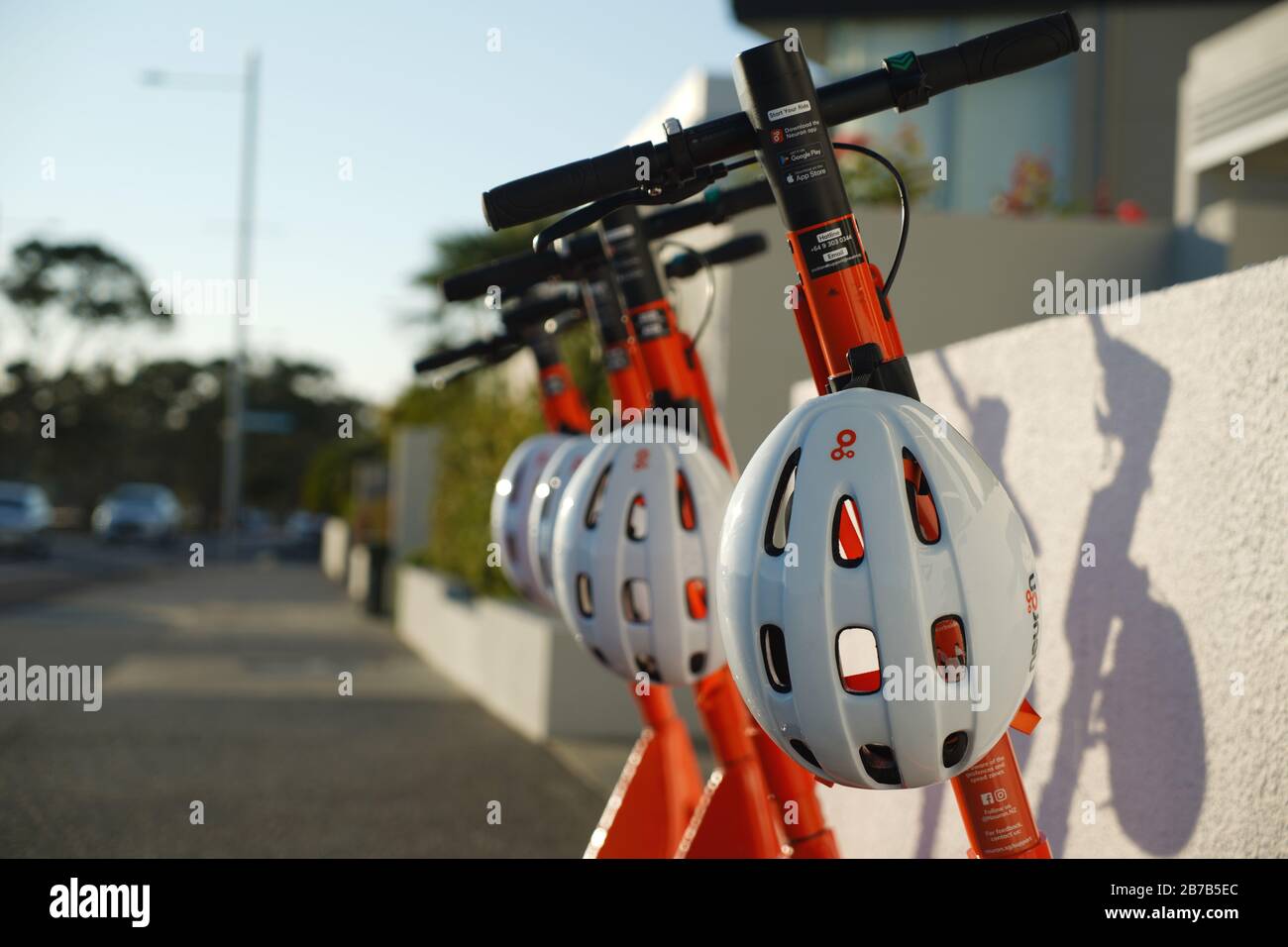 Quatre scooters électriques orange et noir à louer à bord d'un trottoir à Kohimarama, Auckland, Nouvelle-Zélande, avec casques de protection blancs. Banque D'Images
