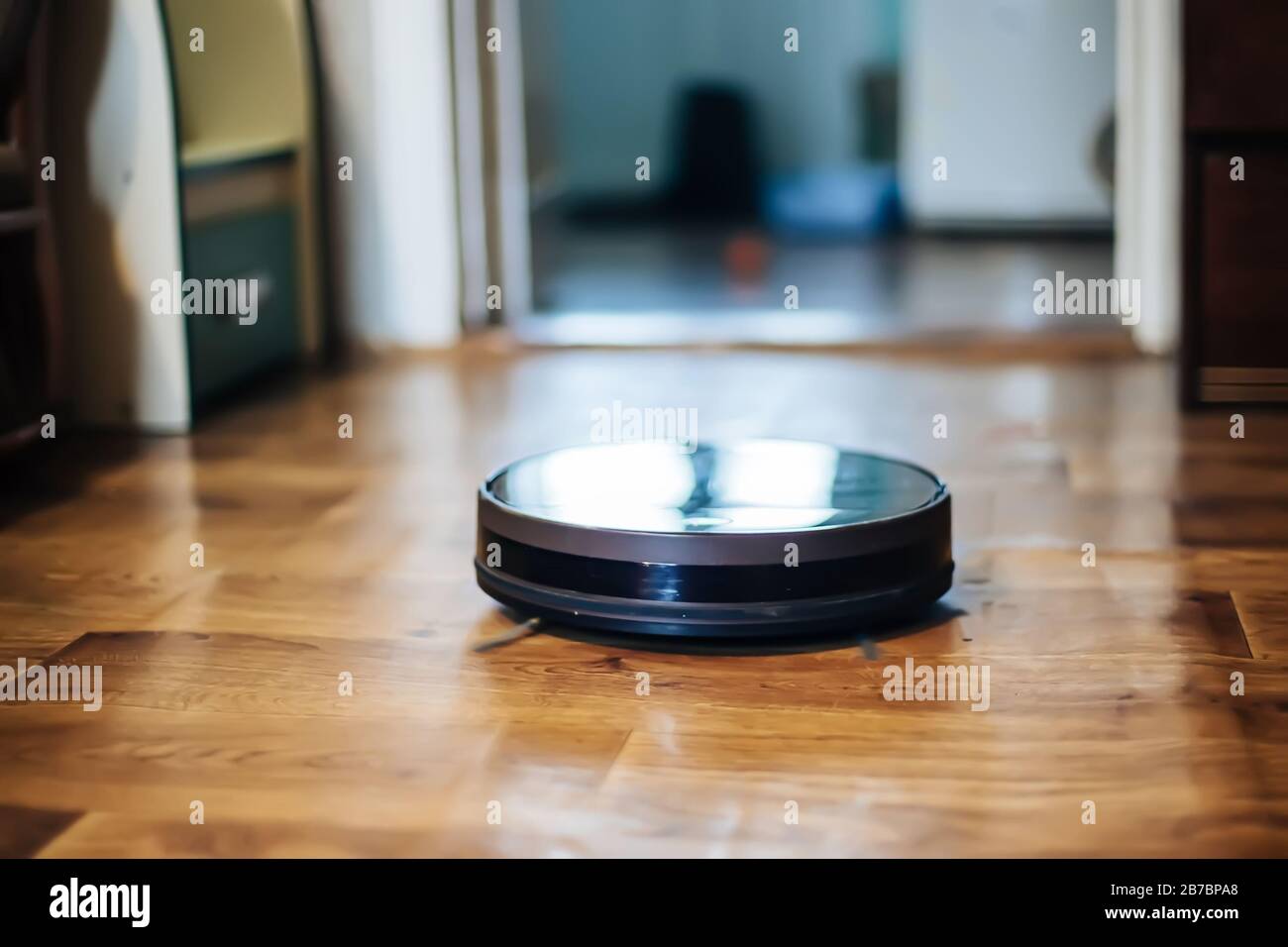 le robot-aspirateur élimine la poussière dans la pièce sur le sol brun.  aspirateur dans l'appartement ordinaire près des chaises. appareil sans fil  domestique moderne pour nettoyer Photo Stock - Alamy