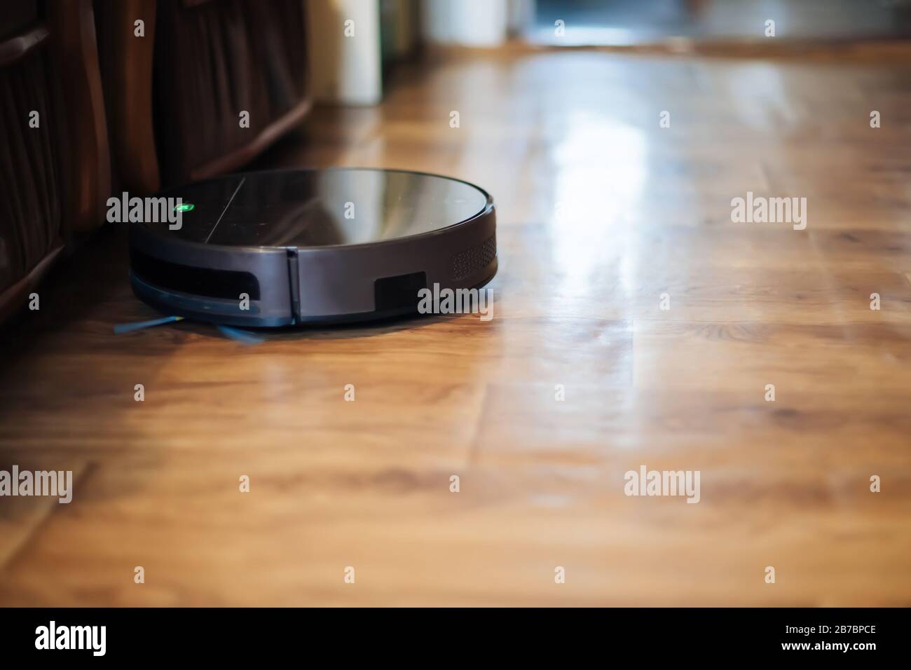 le robot-aspirateur élimine la poussière dans la pièce sur le sol brun. aspirateur dans l'appartement ordinaire près des chaises. appareil sans fil domestique moderne pour nettoyer Banque D'Images