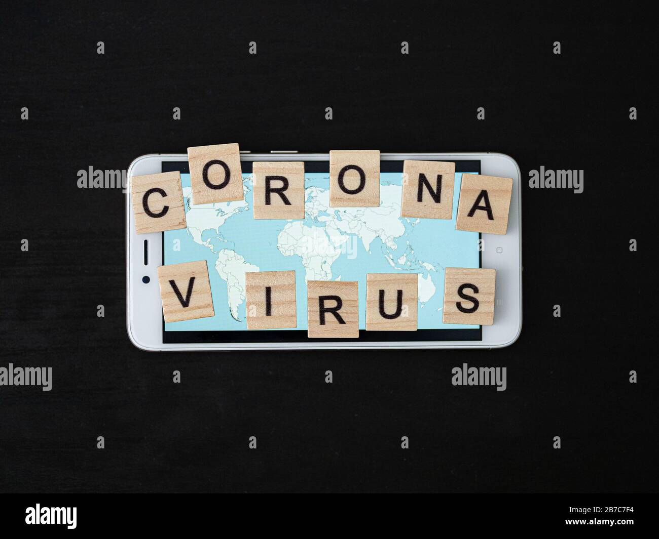 Mot coronavirus en bloc de bois et carte du monde sur l'écran du smartphone. Coronavirus texte sur l'atmosphère dramatique table en bois noir. Vue de dessus du concept de coronavirus. Banque D'Images
