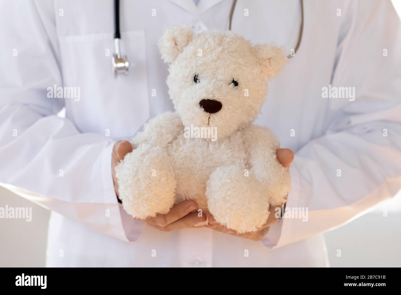 Jeune pédiatre en manteau blanc tenant le jouet dans les mains. Banque D'Images