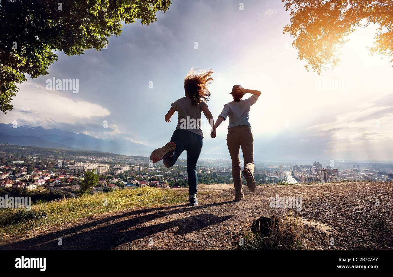 Deux amis tenant les mains et courir à la vue magnifique du panorama de la ville dans les montagnes au coucher du soleil dramatique pluvieux Banque D'Images