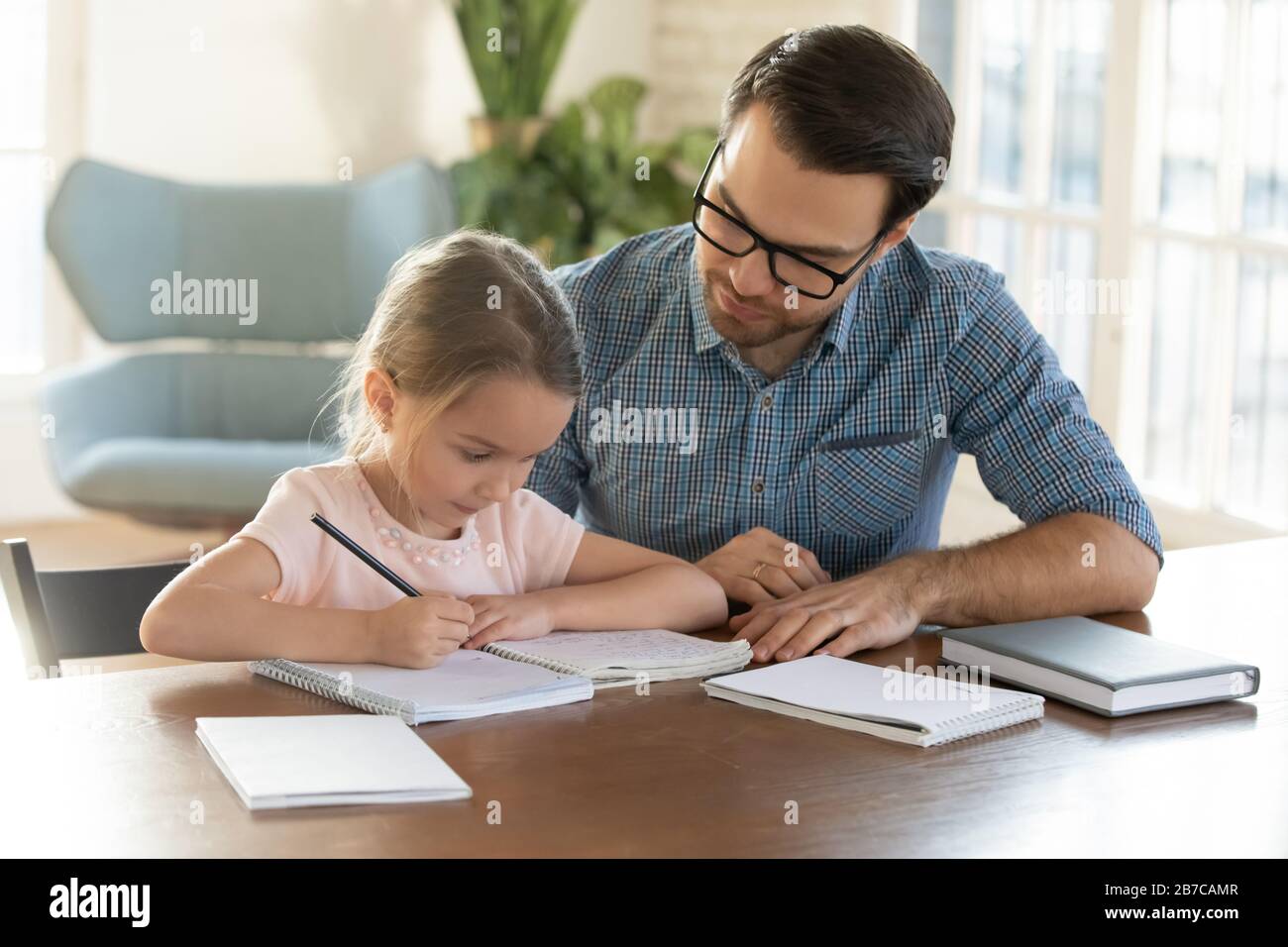 Jeune père bienveillant aidant petite fille à faire ses devoirs. Banque D'Images