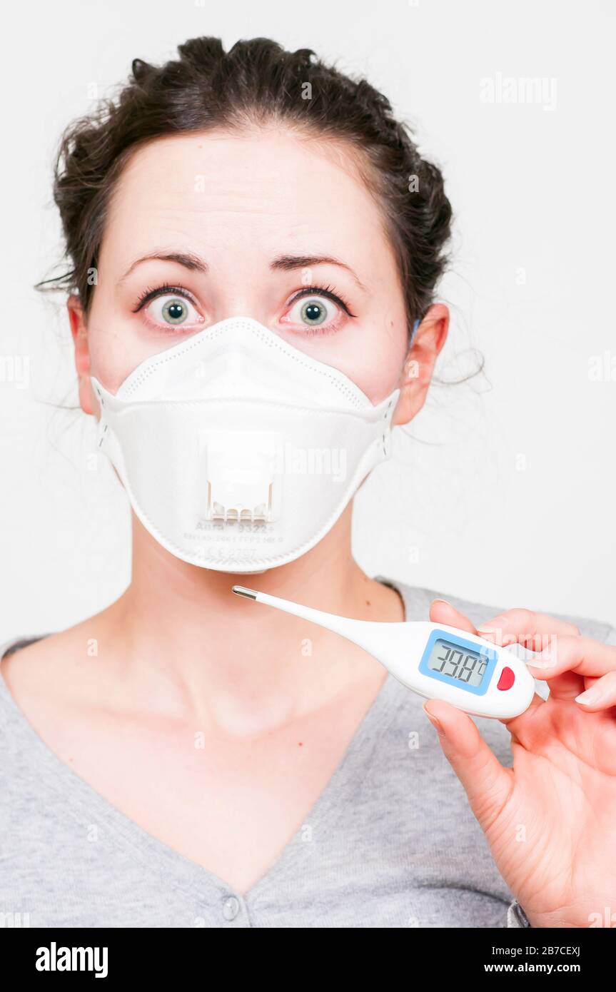 Femme de brunette caucasienne dans un masque médical protecteur sur le visage SRAS-CoV-2, Coronavirus, COVID-19. Avec thermoéther électrique numérique. Fond blanc. Banque D'Images