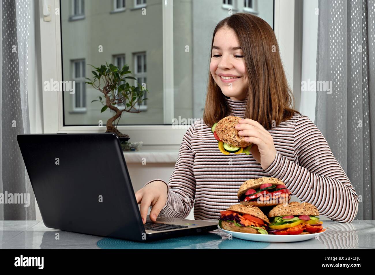 fille utilisant un ordinateur portable et manger un sandwich végétarien à la maison Banque D'Images