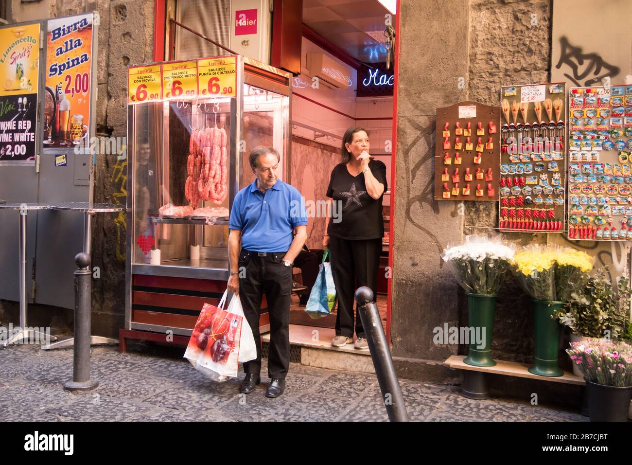 Un couple de personnes âgées est en pause devant un magasin de boucher dans une rue de Naples, en Italie. Banque D'Images