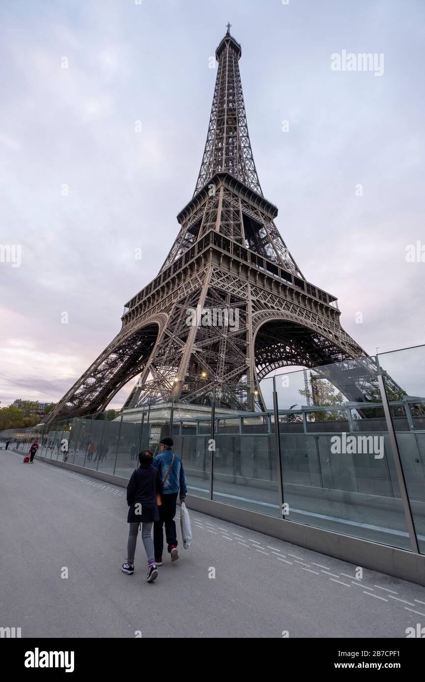 Deux personnes marchant à l'extérieur des barrières de verre anti-terrorisme de la Tour Eiffel à Paris, France, Europe Banque D'Images