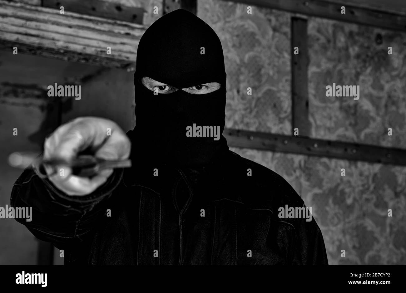 Un homme portant un masque/une capuche dans un bâtiment abandonné. Il pointe un grand couteau vers le visualiseur. Vue rapprochée avec faible profondeur de champ. B&O. Banque D'Images