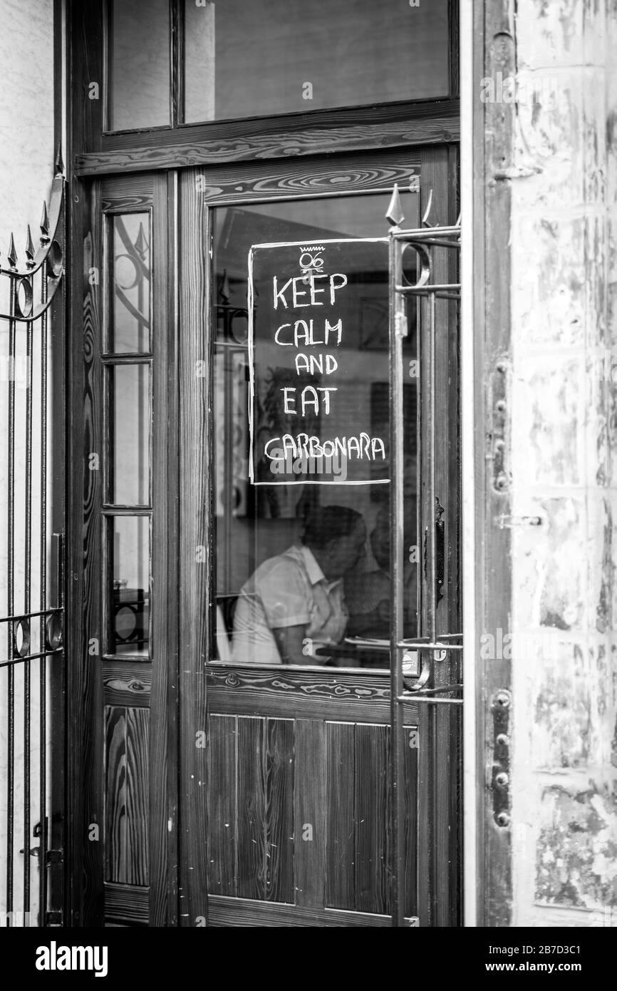 Gros plan vertical noir et blanc d'une fenêtre de restaurant à la Valette, Malte, avec une citation drôle sur la porte du magasin. Banque D'Images