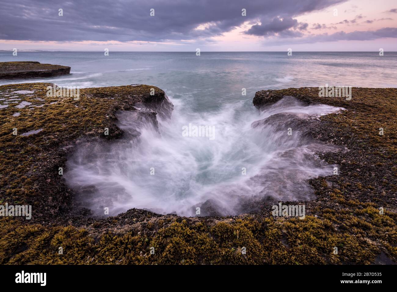 Un magnifique paysage marin doré en fin de soirée avec des rochers au premier plan, photographié un jour de tempête après le coucher du soleil à Arniston, Afrique du Sud. Banque D'Images