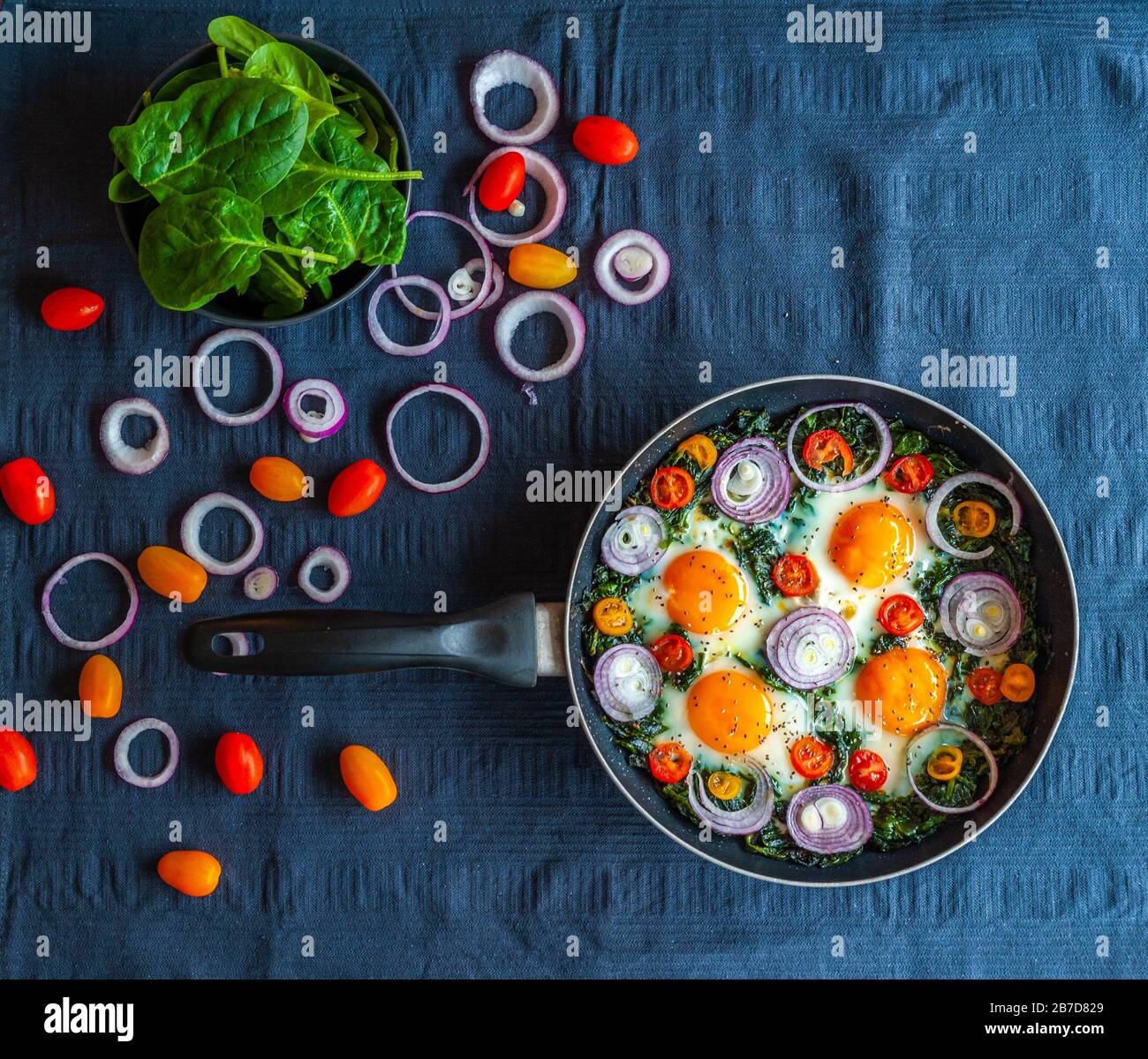 Une omelette aux épinards dans une poêle et décorée d'oignons frais, de tomates et d'épinards Banque D'Images