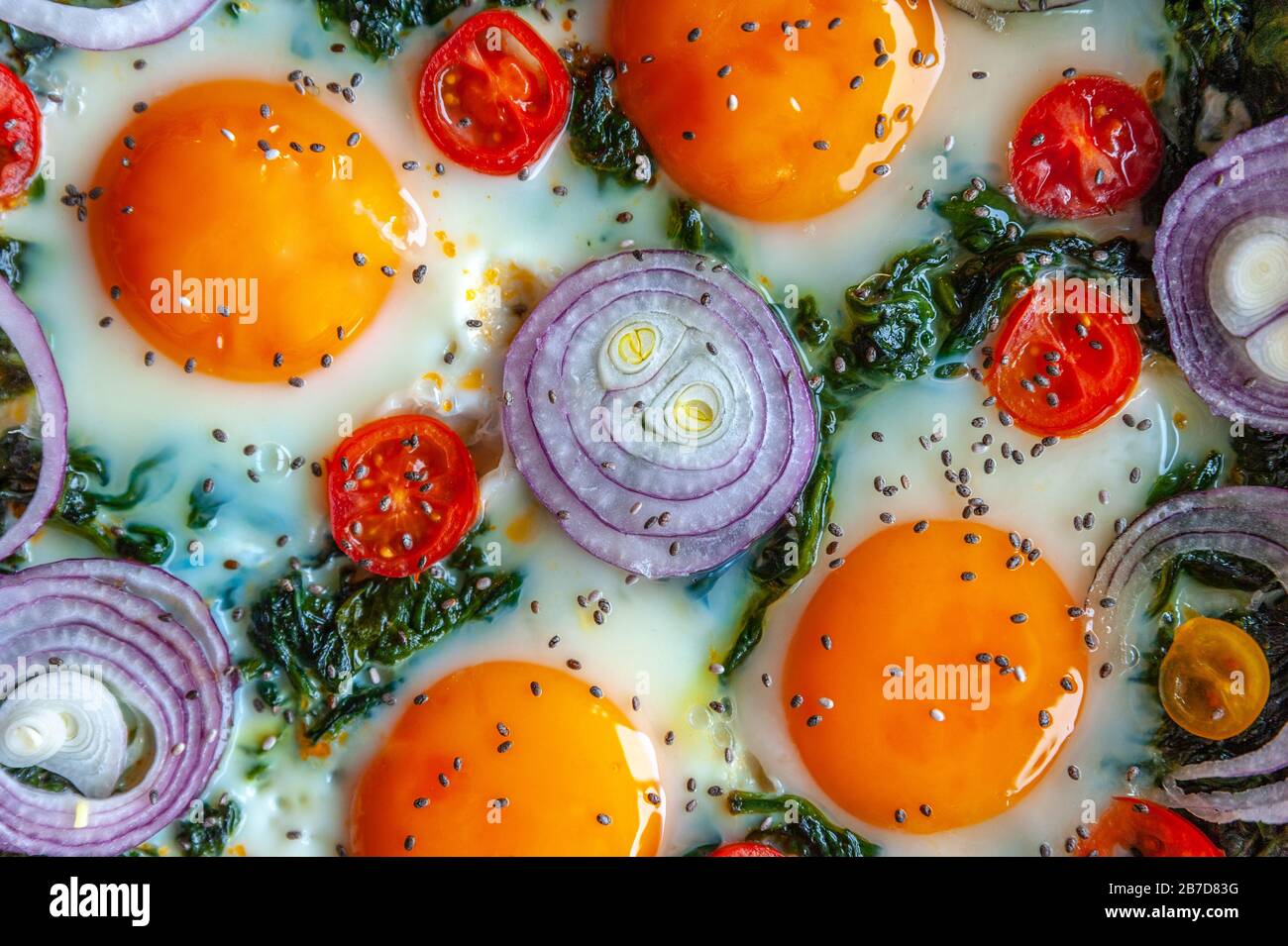 Détail d'une omelette aux épinards dans une poêle et décorée avec de l'oignon frais, des tomates et des épinards Banque D'Images