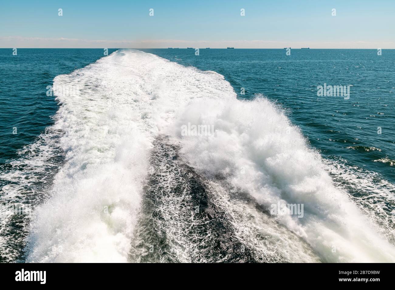 Bateau à voile rapide en mer, sentier derrière bateau sur l'eau. Ciel bleu sans nuages, horizon clair. Banque D'Images