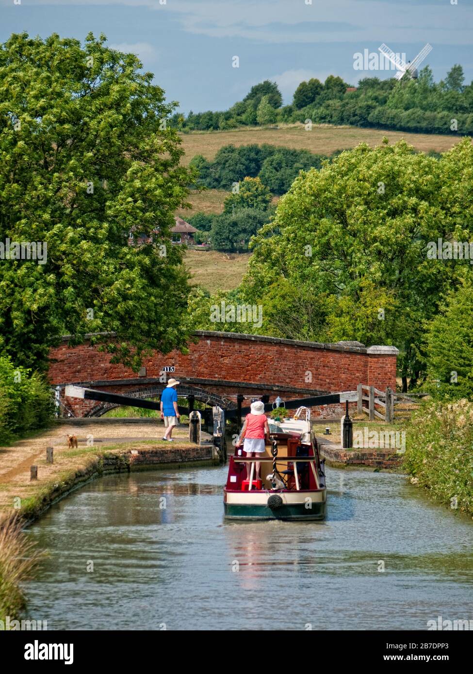 Bateau de plaisance approchant une écluse sur le vol Napton du canal Oxford (Sud), Oxfordshire, avec moulin à vent derrière à Napton on the Hill, Angleterre, Royaume-Uni, Banque D'Images