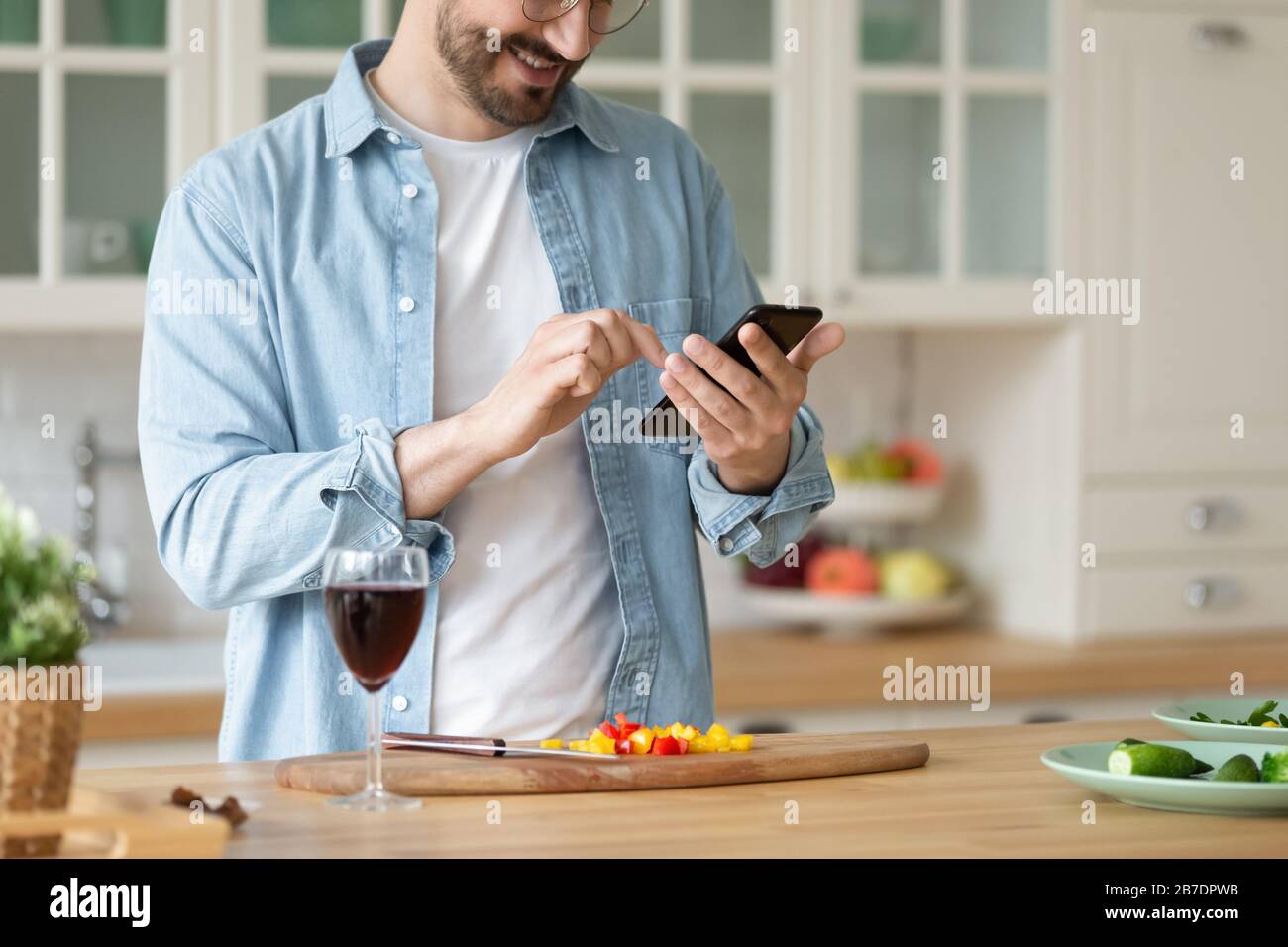 Homme souriant à l'aide d'un smartphone, salade de cuisson, préparation des légumes Banque D'Images