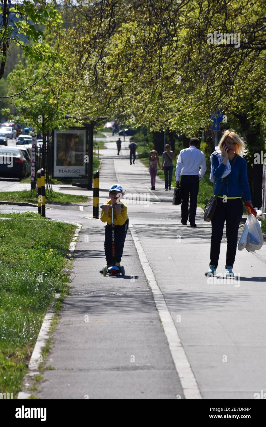 Une femme parle au téléphone avec un garçon sur un scooter. Les gens marchent une journée ensoleillée. Banque D'Images