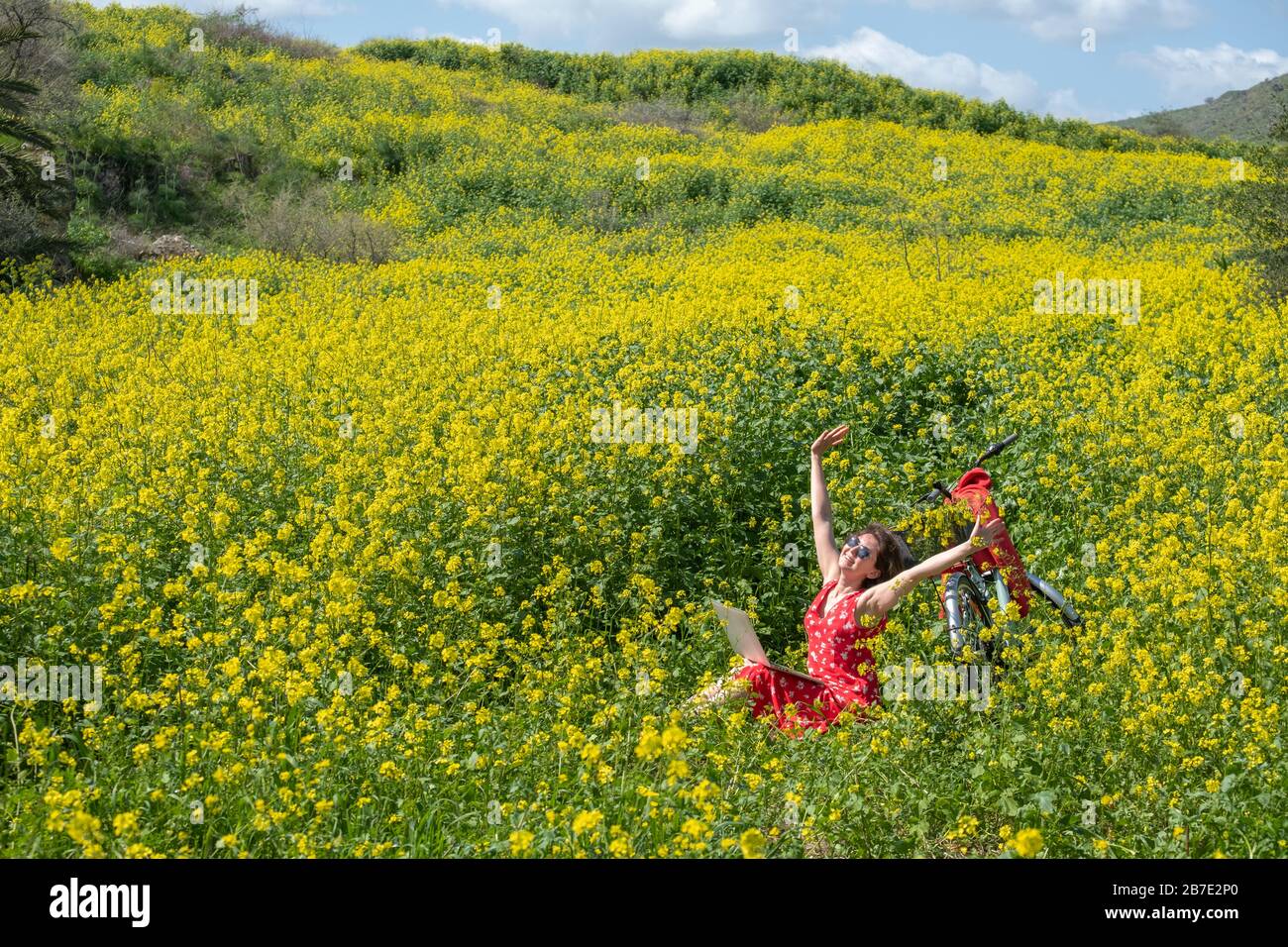 Une fille indépendante travaille derrière un ordinateur portable dans une fleur de printemps et un champ ensoleillé. La fille est venue sur le terrain sur un vélo et il est debout à côté d'elle Banque D'Images