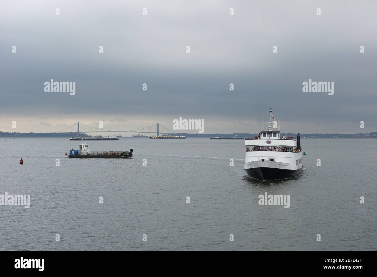 Bateau de croisière de la Statue de la liberté V et divers autres navires sur le fleuve Hudson en journée nuageux avec le pont Verrazzano Narrows en arrière-plan Banque D'Images