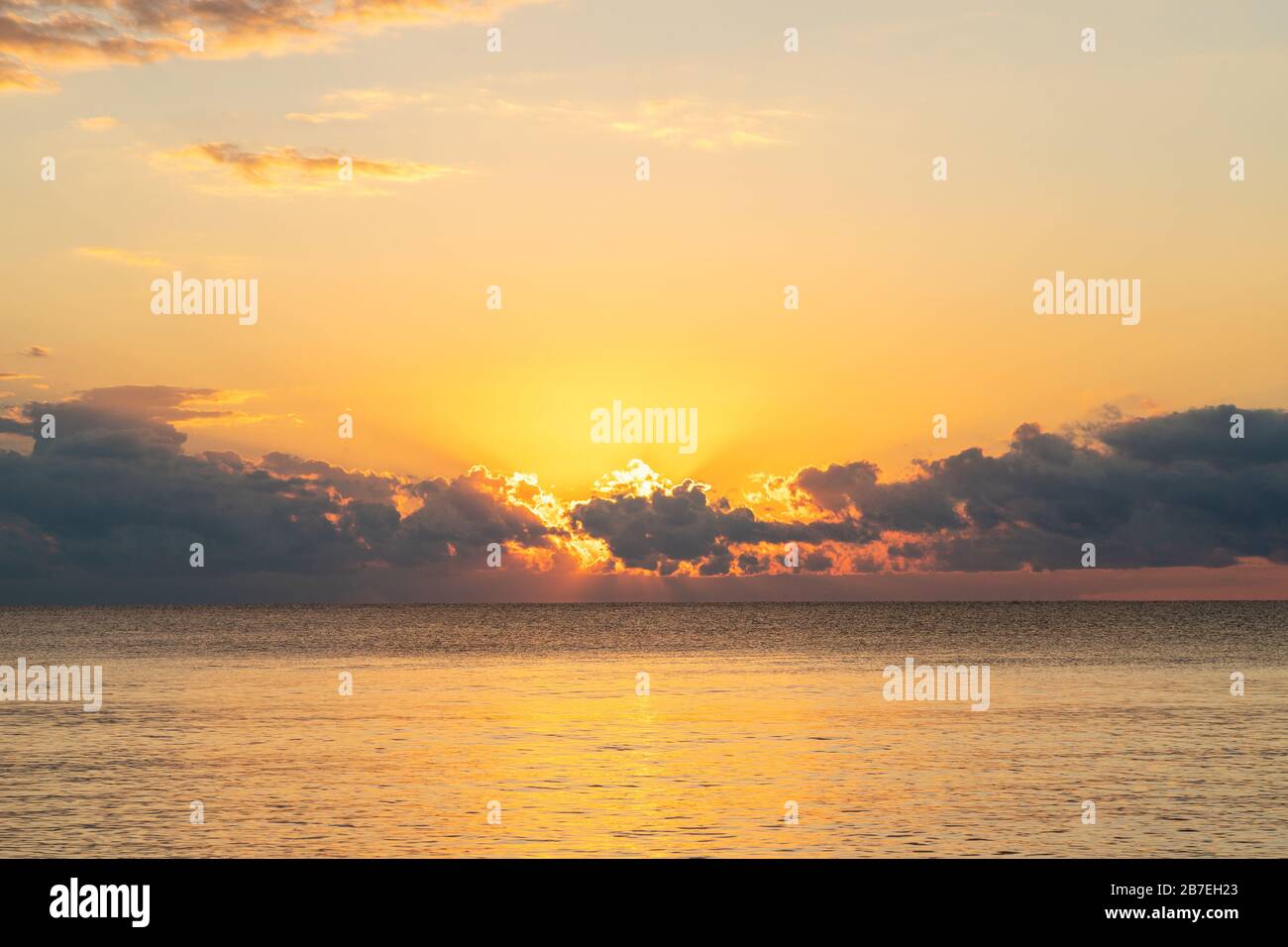 Lever de soleil doré se brisant des nuages au-dessus de la mer des Caraïbes comme vu des rives de la Riviera Maya à Cancun, au Mexique. Banque D'Images