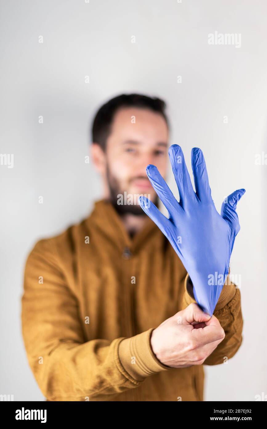 Jeune homme mettant sur un gant en latex bleu. Photo de ton commercial axée sur le monde du nettoyage ou de la médecine. Banque D'Images
