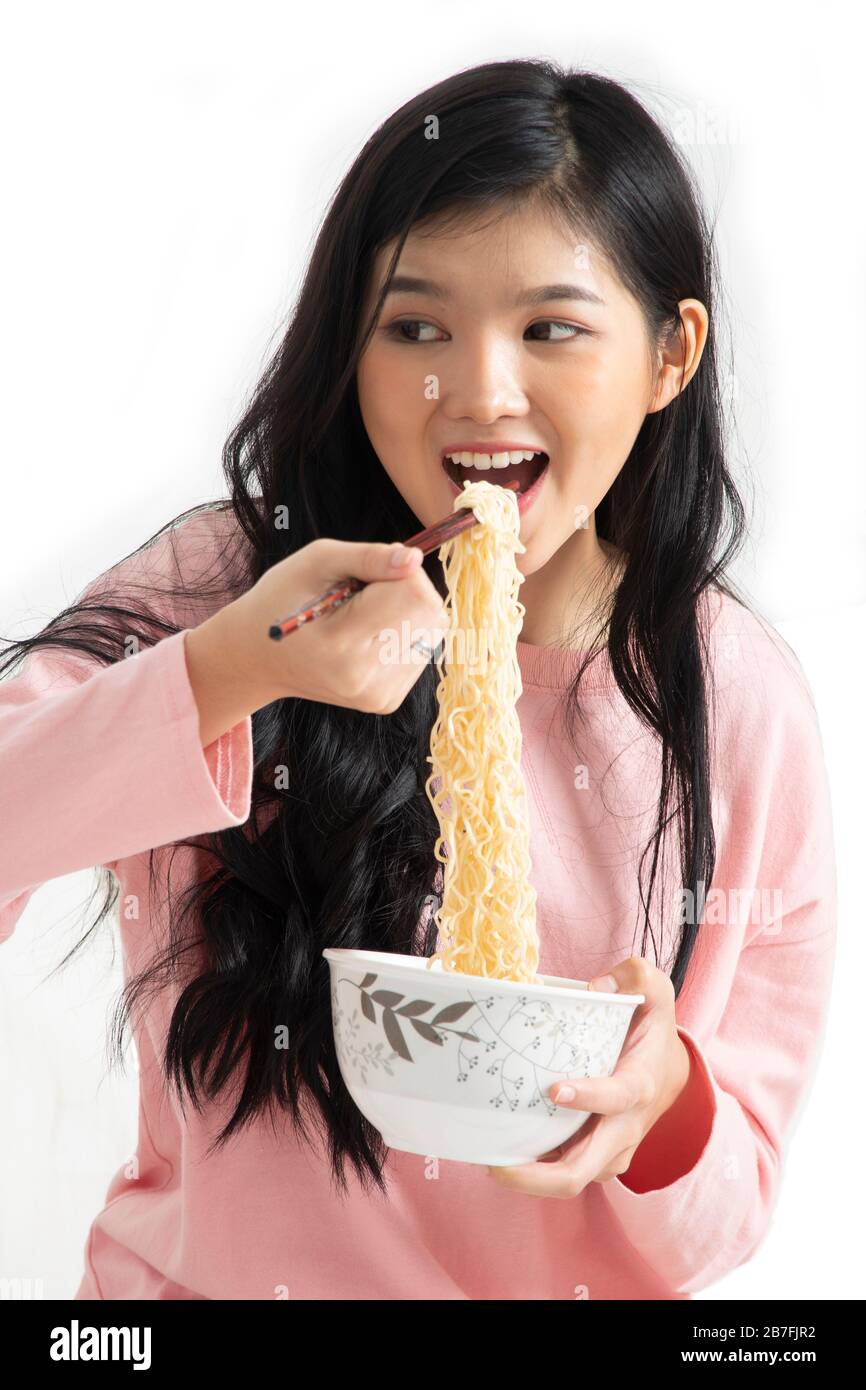 La fille aime manger tout en utilisant des baguettes pour tenir des nouilles instantanées dans sa bouche sur fond blanc. Banque D'Images