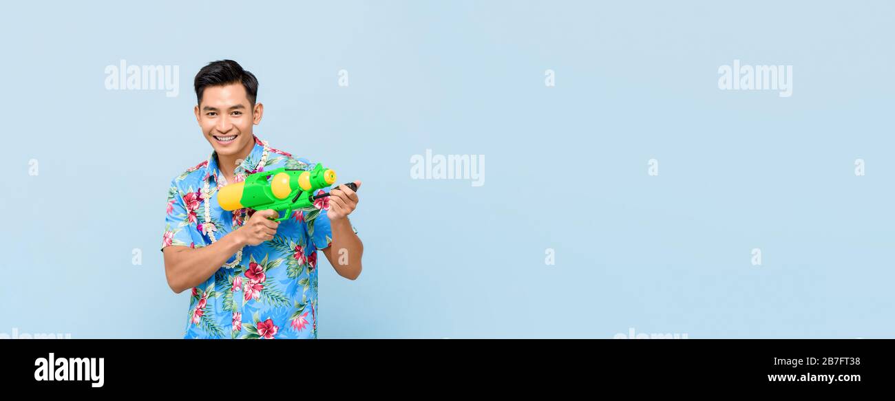 Homme asiatique souriant jouant avec un pistolet à eau isolé sur fond bleu bannière avec espace de copie pour le festival Songkran en Thaïlande et au sud-est A. Banque D'Images