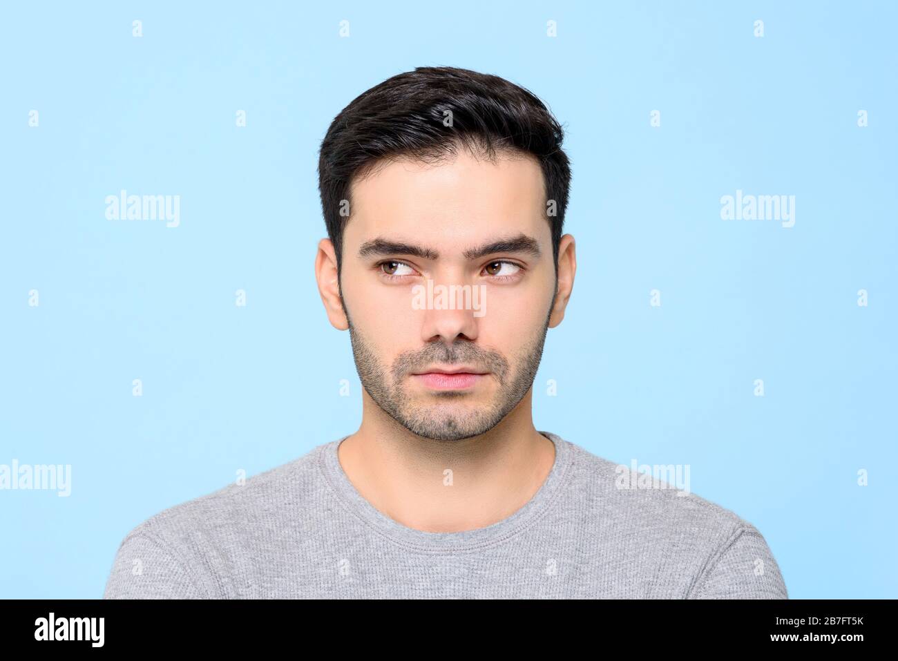 Gros plan portrait de bel homme pensant avec les yeux regardant latéralement isolé sur fond bleu de studio Banque D'Images