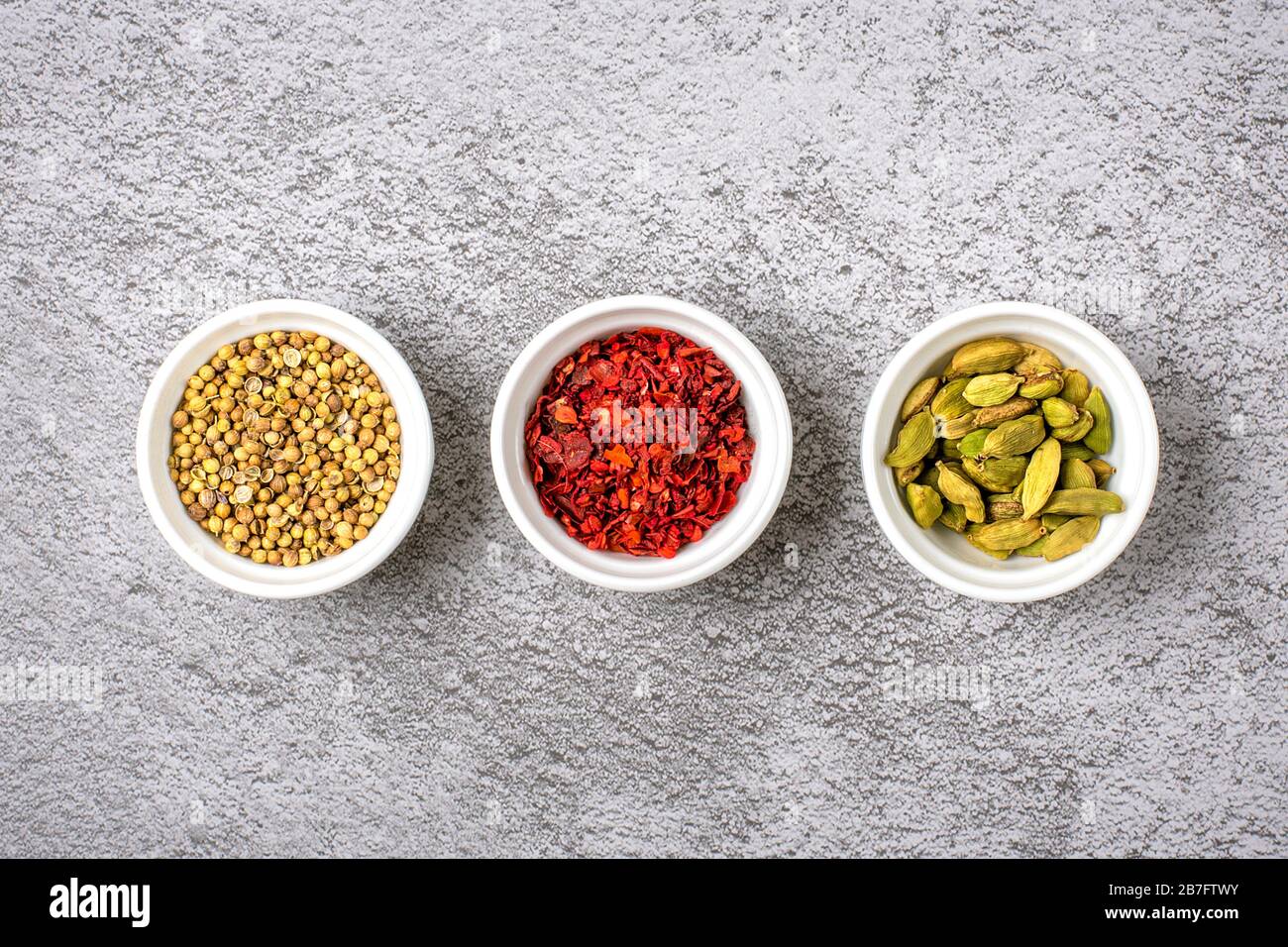 Mélange d'épices aromatiques coriandre, bergamote, paprika en tasses blanches sur un fond gris en béton vue dessus plat laïque nourriture saine. Banque D'Images