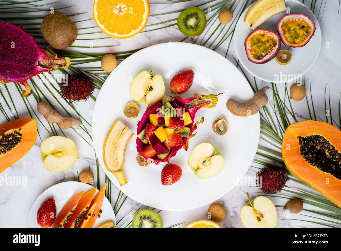 Vue de dessus des assiettes avec des fruits tranchés. Assortiment de différents fruits exotiques avec des feuilles tropicales sur fond de marbre. Délicieux en-cas, vitamine healt Banque D'Images