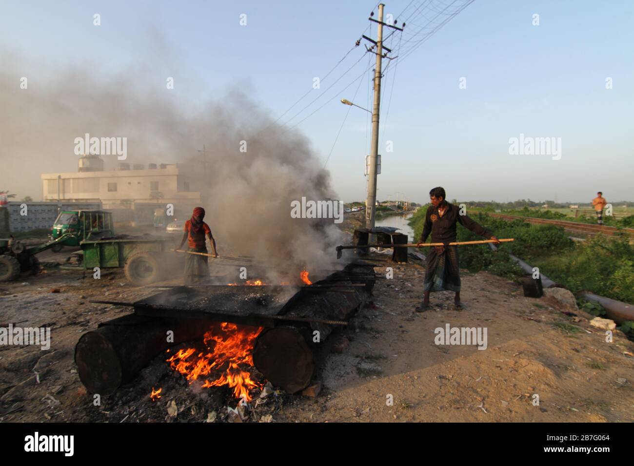 Les ouvriers de la construction chauffent des bitumeux dans une journée chaude ensoleillée d'été sans masque de protection approprié ou gants à main dans l'extrême fumée. Banque D'Images