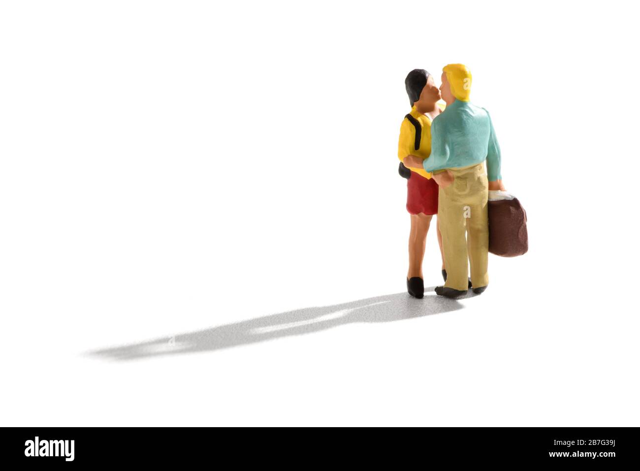 Les amateurs miniatures baisseront à l'arrivée ou au départ avec un jeune homme et une femme embrassant comme il porte une grande valise pour voyager sur blanc avec des feuilles de feuilles Banque D'Images