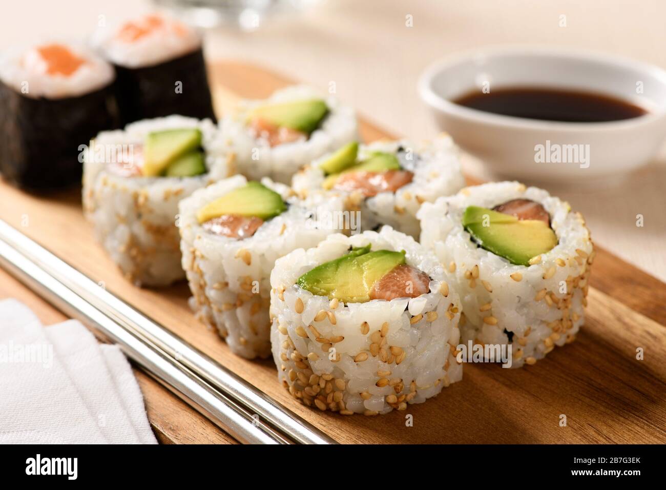 Gros plan sur une portion de rouleaux de sushis uramaki avec de la poire et du saumon avocat frais au nori et du riz roulé dans des graines de sésame sur un plateau en bois à la table Banque D'Images
